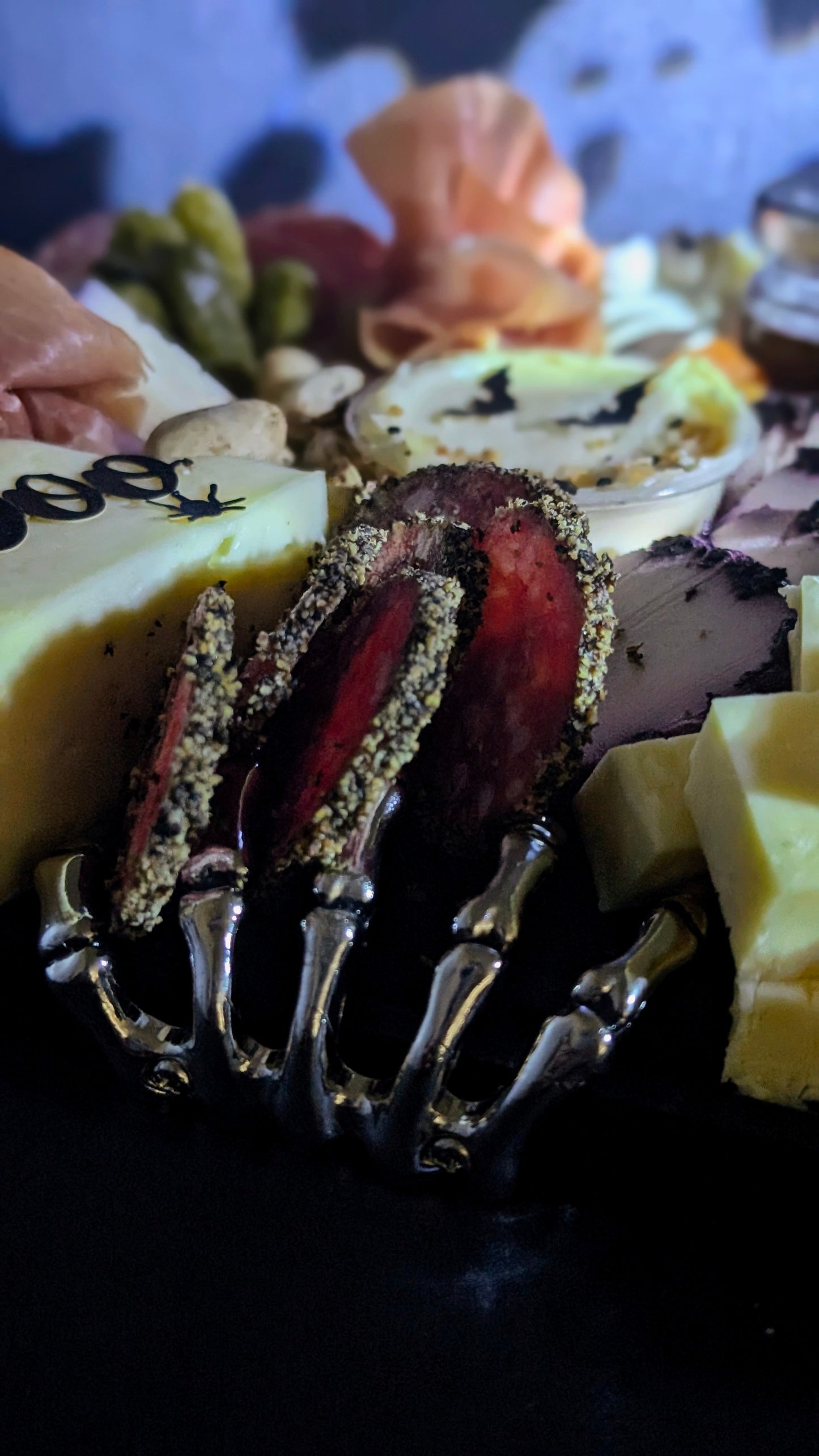Close-up of a charcuterie board with various meats and cheeses, including silver skeleton hand. 